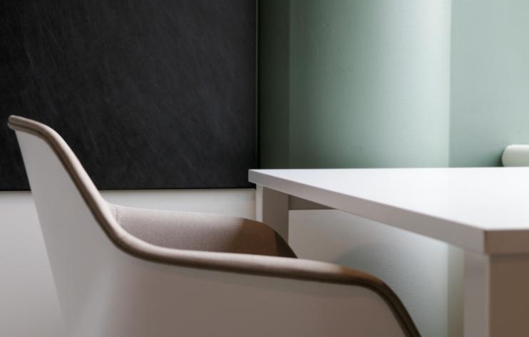 Närbild på en vit stol vid ett bord och en ljusgrön vägg i bakgrunden.